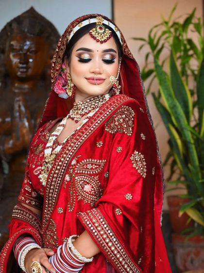 A beautiful bride in a red velvet lehenga. The makeup features a soft cut-crease eye and a flawless base.