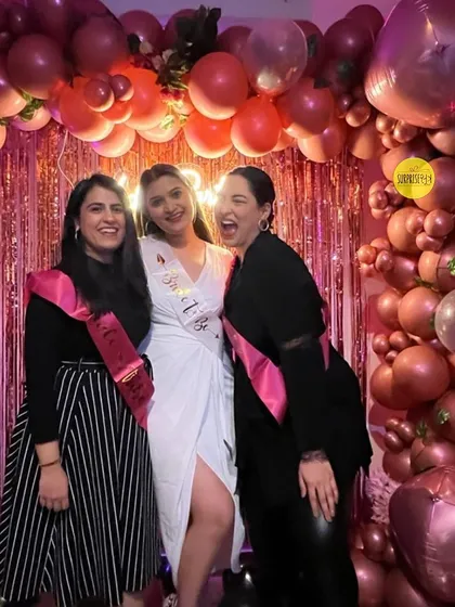 A fun and chic bachelorette party setup. The bride-to-be and her friends pose in front of a backdrop made of a metallic fringe curtain and a dramatic arch of chrome pink balloons.