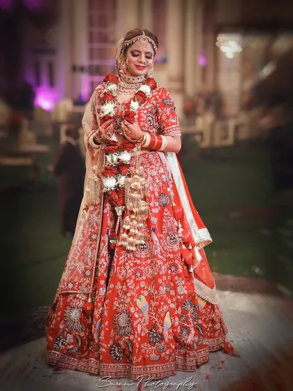 A full-length outdoor portrait of the bride in her intricately embroidered red lehenga.