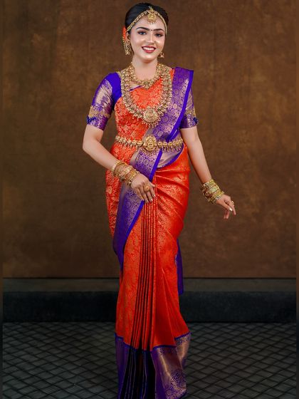 An orange and royal blue Kanchipuram saree styled for a photoshoot. The contrast is striking, and the drape is kept traditional to highlight the saree's grandeur.