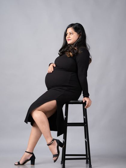 A modern and chic solo maternity pose. This seated portrait in a stylish black dress shows off the baby bump beautifully.