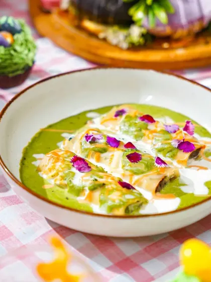 A comforting bowl of cannelloni in a green sauce, garnished with cream and edible flowers. This dish, part of our Easter spread, looks both elegant and inviting against the pastel checkered tablecloth.