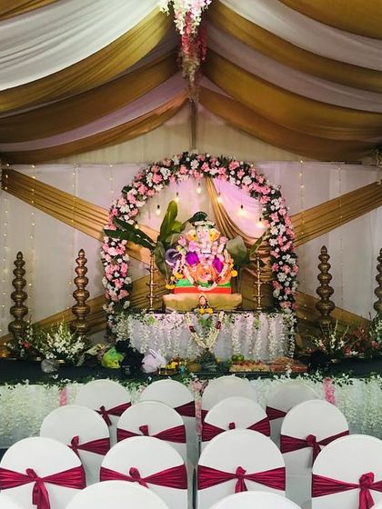 A wider view of the seating arrangement for the Ganesh Chaturthi festival. The chairs are adorned with red sashes, and the tent ceiling is draped with flowing fabric, creating a festive and cohesive look.