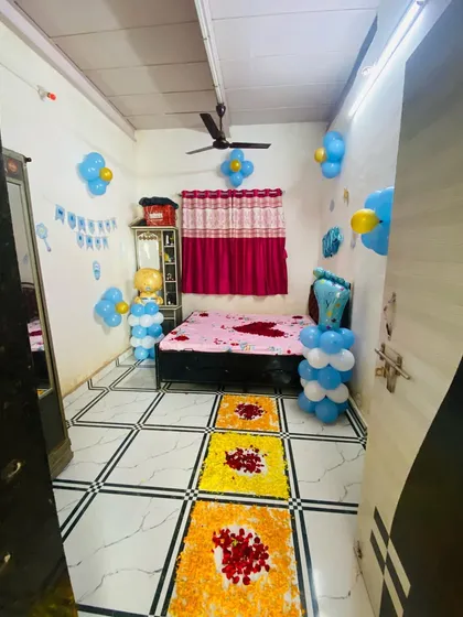 A room decorated for a baby boy's welcome, with blue and white balloon arrangements and flower rangoli.