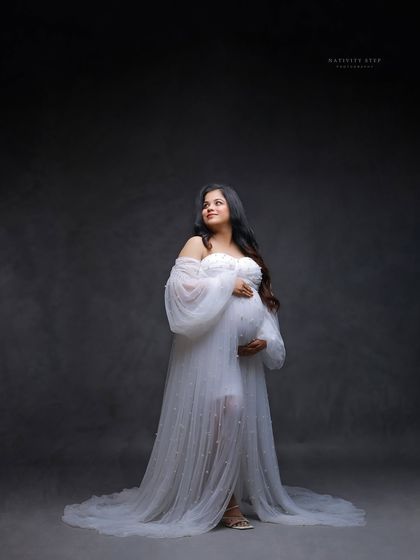 A graceful solo portrait of the mother-to-be in a white gown. Her upward gaze and the soft lighting create a hopeful and serene mood.