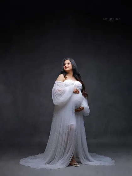 A graceful solo portrait of the mother-to-be in a white gown. Her upward gaze and the soft lighting create a hopeful and serene mood.