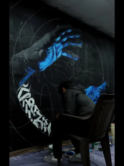 A work-in-progress shot of the calligraffiti hands mural. Here you can see me sitting and planning the next steps, with the powerful blue hands already taking shape on the wall.