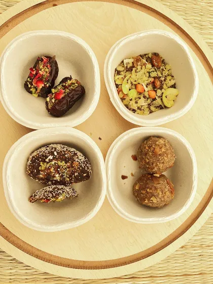 A sampler plate showcasing some of my favorite treats. It features stuffed dates, millet salad, energy laddus, and a chocolate-covered treat, all served in eco-friendly bowls.
