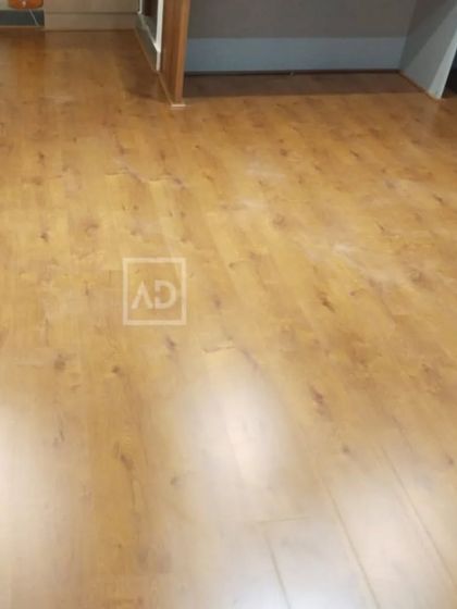 A wide shot of a completed wooden flooring project in a large room. The light reflects beautifully off the surface, showcasing the quality and texture of the material.
