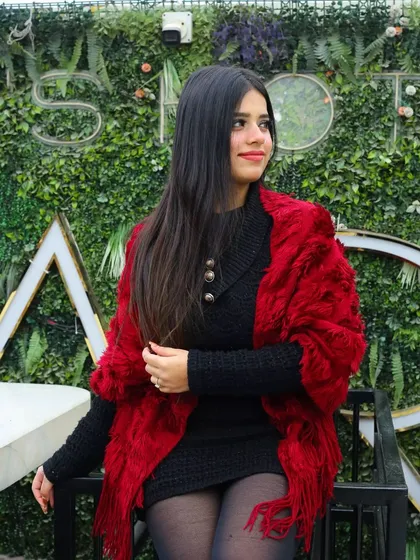A relaxed, seated portrait against a green wall. The contrast between the red outfit and the green background makes the colors pop, creating a visually striking winter fashion shot.
