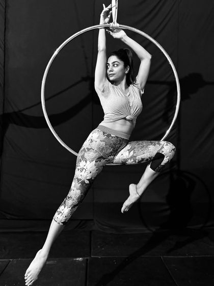 A student strikes a dynamic, poised pose on the aerial hoop. This black and white shot highlights the elegant lines and muscular engagement required.