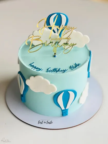 A whimsical hot air balloon themed cake. The light blue buttercream sky, fluffy clouds, and a golden "Happy Birthday" topper make it a delightful choice for a child's celebration.