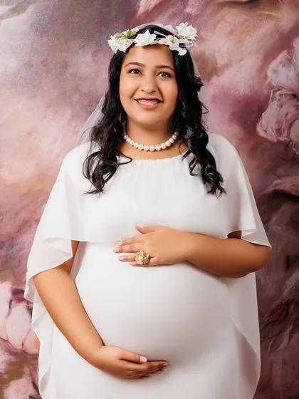 Sometimes, simplicity is the most elegant statement. This classic maternity portrait features a beautiful mother-to-be in a simple white gown and a delicate floral headpiece. The focus is entirely on her serene expression and the miracle she is creating.
