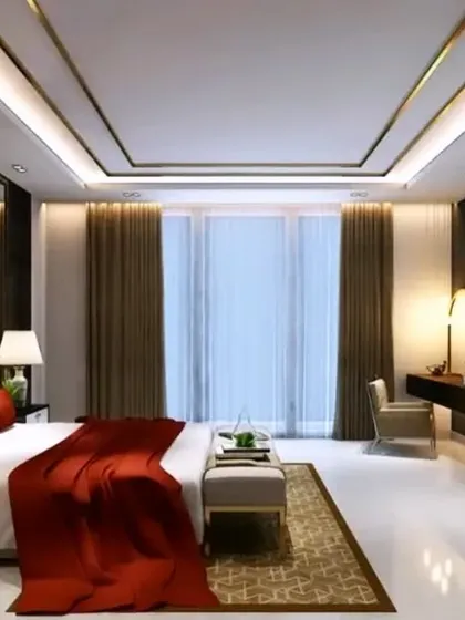 A luxurious bedroom featuring a tray ceiling with gold trim and cove lighting. The design is completed with rich red and gold fabrics, a sleek dressing table, and elegant curtains that create a grand and opulent feel.