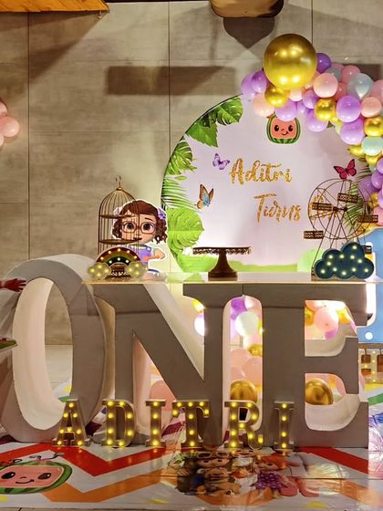 A Cocomelon-themed first birthday with a large 'ONE' table. The setup includes character cutouts, a themed backdrop, and a colorful balloon garland.