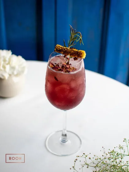 The 'Rose Merry' cocktail, a beautiful blend of floral and herbal notes. The charred pineapple and rosemary garnish adds a smoky complexity.