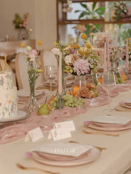 An elegant tablescape for an anniversary brunch. The table features dusty pink plates, a soft velvet runner, and delicate centerpieces of wildflowers, creating a romantic and sophisticated setting.
