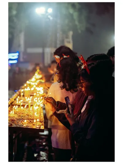 A group of people lighting candles at the Sacred Heart Cathedral. The image focuses on the rows of flickering flames, symbolizing hope and collective prayer during the Christmas season.