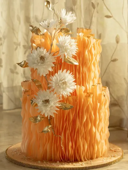 This two-tier cake is from my Ruffle Paper Collection, featuring vibrant orange wafer paper ruffles that look like fabric. I finished it with delicate white sugar flowers and touches of edible gold leaf for a modern, artistic look.
