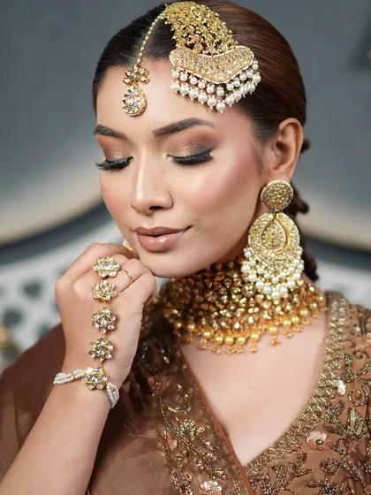 The bride's elegant pose highlights her sophisticated braided hairstyle and stunning gold jewelry, perfect for a Nikah or Walima ceremony.
