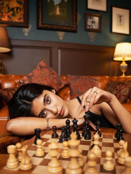 A creative and strategic fashion shot using a chessboard as a prop. The model's pose and the game in progress add an intellectual and intriguing layer to the visual story.