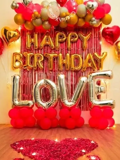 A romantic birthday backdrop with a 'LOVE' theme. This setup combines a 'Happy Birthday' foil banner over a shimmer curtain with large 'LOVE' foil letters and a floor heart made of rose petals.