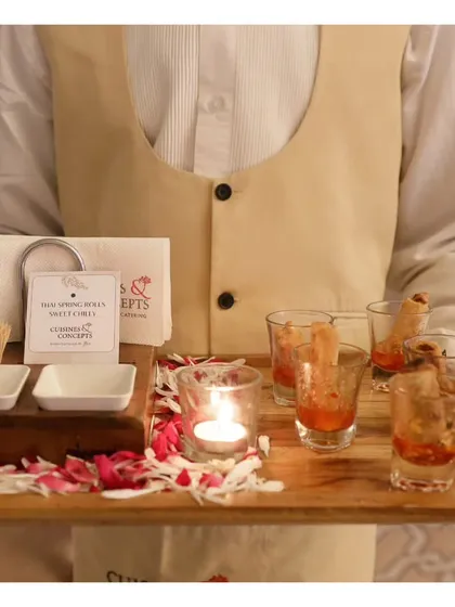 A server presents a tray of Thai spring rolls served in shot glasses with a sweet chili dip. This creative presentation is both visually appealing and practical for a mingling crowd.