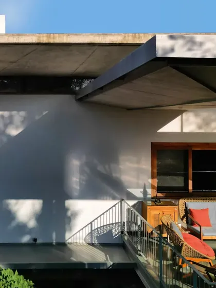Dappled light from nearby trees plays across the white walls and under the deep overhang of a concrete canopy.