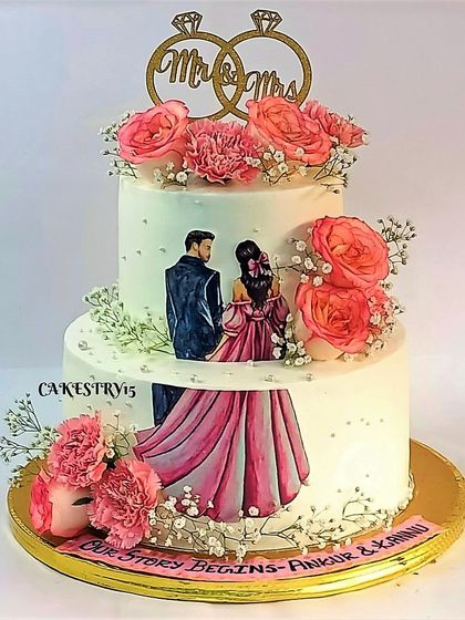 A romantic two-tier anniversary cake featuring an edible print of the couple. The cake is beautifully decorated with fresh pink roses, carnations, and a "Mr & Mrs" topper.
