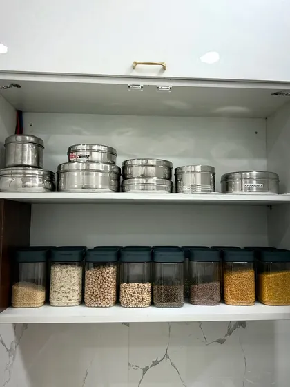 A practical cabinet setup with steel containers for bulk items on the top shelf and clear jars for daily-use dals below. This hybrid system is tailored to the client's specific needs.