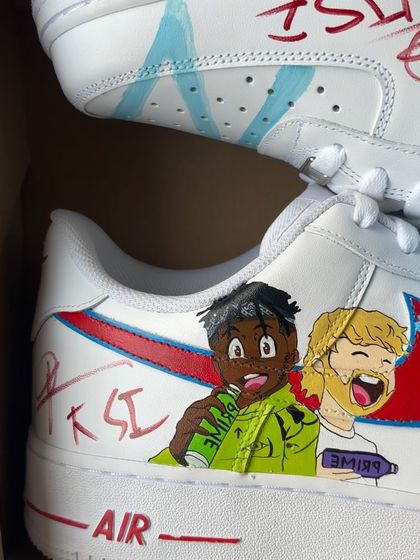 A close-up of the signed sneaker, featuring cartoon versions of KSI and Logan Paul with their Prime and Feastables brands.