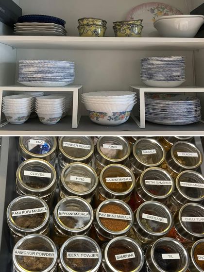 A combined view of an organized crockery cabinet using risers and a perfectly arranged spice drawer below it.
