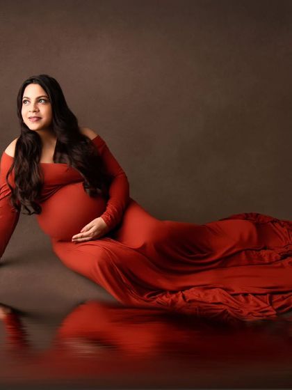 An artistic portrait with a beautiful reflection effect. The mom-to-be is lying gracefully in a burnt-orange gown.
