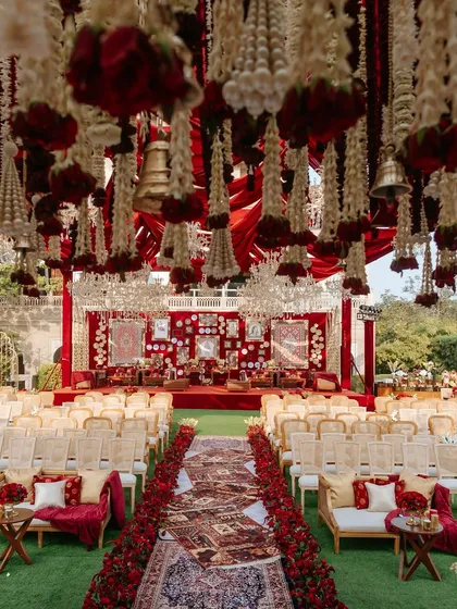 A view of the 'Laal Ishq' wedding ceremony setup from the guest's perspective. The combination of hanging floral strings, a rich red backdrop, and traditional seating created an immersive and culturally rich experience.