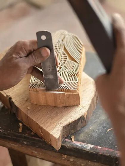 The heart of our craft lies in the hands of our master carvers. Here, an artisan chisels away at a piece of teak wood, bringing an intricate design to life. This level of detail and skill is what makes each print a unique piece of art.