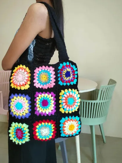 Modeling the rainbow granny square tote bag to show its generous size. It's perfect as a market bag or everyday carry-all.