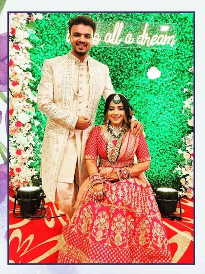 A beautiful couple posing against a vibrant green backdrop. Her red and gold lehenga perfectly complements his elegant ivory sherwani.