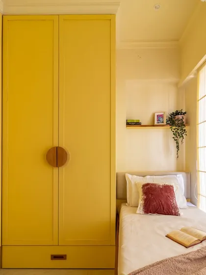 The full-height yellow wardrobe with unique wooden handles maximizes vertical storage while adding a bold design statement to this compact room.