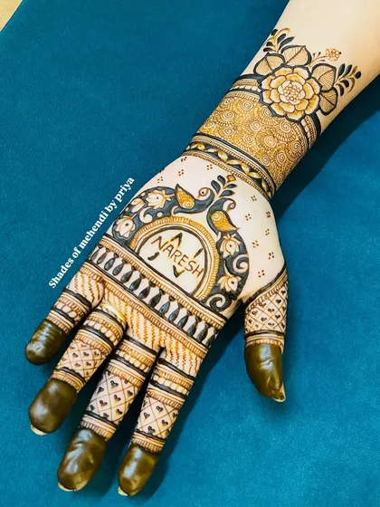 A simple yet elegant groom mehendi design. The groom's name, 'Naresh', is written inside a decorative circle surrounded by peacock motifs on the back of the hand.