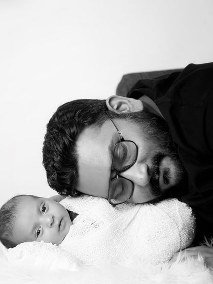 A father and his newborn share a quiet moment in this beautiful black and white portrait. The high-contrast lighting creates a simple yet powerful image.
