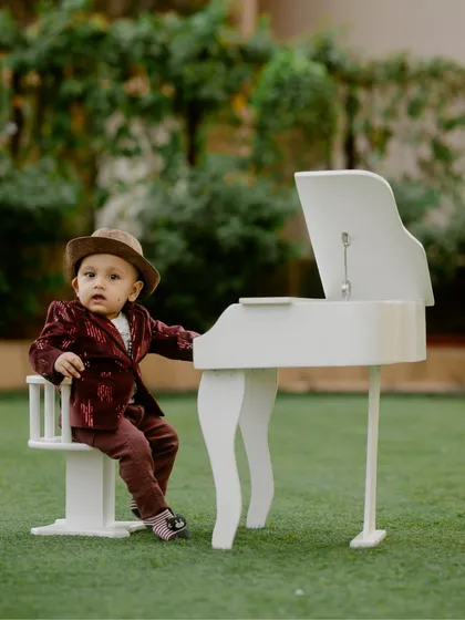 A handsome little musician posing by his miniature piano during an outdoor milestone photography session.