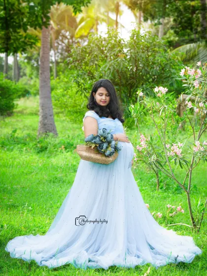 A dreamy solo portrait in a flowing light blue gown. The mother-to-be holds a basket of matching flowers, adding a touch of whimsy to this garden photoshoot.