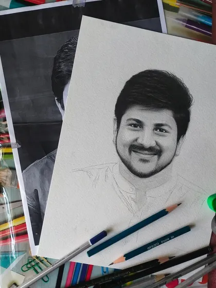 This flat lay shot shows a portrait in progress, surrounded by the tools of my trade. You can see the reference photo, my graphite pencils, an eraser, and a sharpener, all essential for my work.