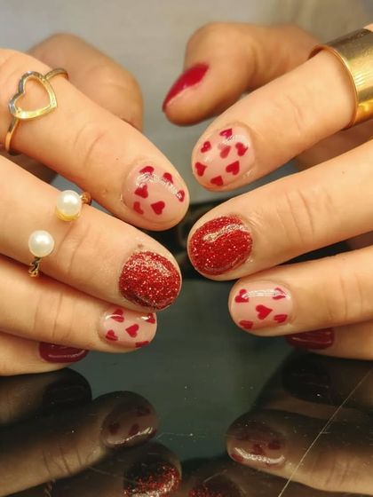 A fun and festive manicure with red glitter accent nails and sheer nails covered in tiny red hearts.