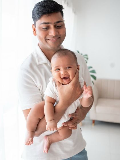 A proud father holding his smiling baby. The natural light from the window creates a soft, beautiful portrait.