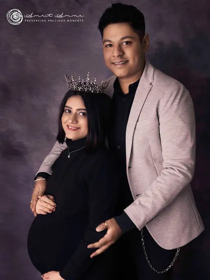 A chic and modern studio portrait. The couple's coordinated dark outfits and the queenly crown create a look of sophisticated elegance as they await their twins.