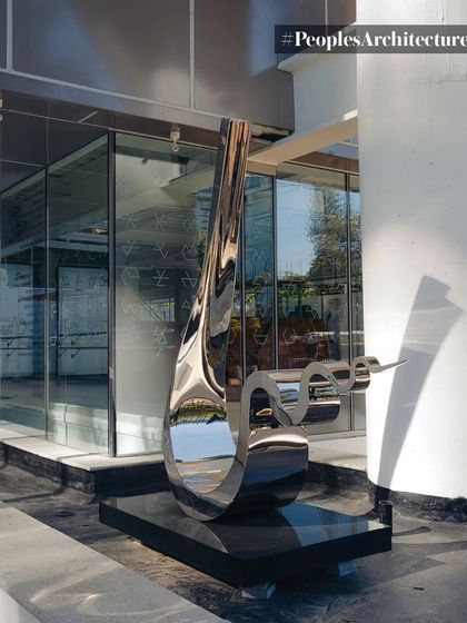 A close-up of the "Spill" sculpture by Tarik Currimbhoy at the entrance of MAP, with the building's architecture as a backdrop.