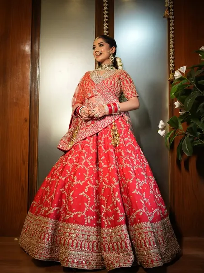 A full view of a classic bridal look. The hair is styled into a traditional bun, providing a graceful foundation that supports the dupatta and enhances the overall silhouette of the bridal lehenga.