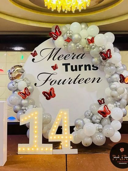 A chic and simple circular backdrop for a 14th birthday, decorated with white and silver balloons and red butterflies.