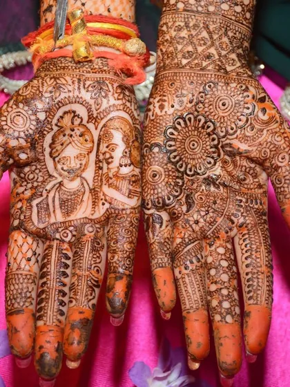 The rich, orange stain of a bridal mehndi featuring a bride and groom portrait. The surrounding patterns are dense and traditional, filling the entire hand.